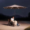 A man playing with his dog under the 9ft Round Tilt Patio Umbrella with Solar LED Light on the beach